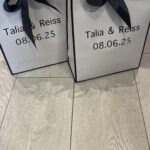 Two black gift bags with ribbons on a wooden surface