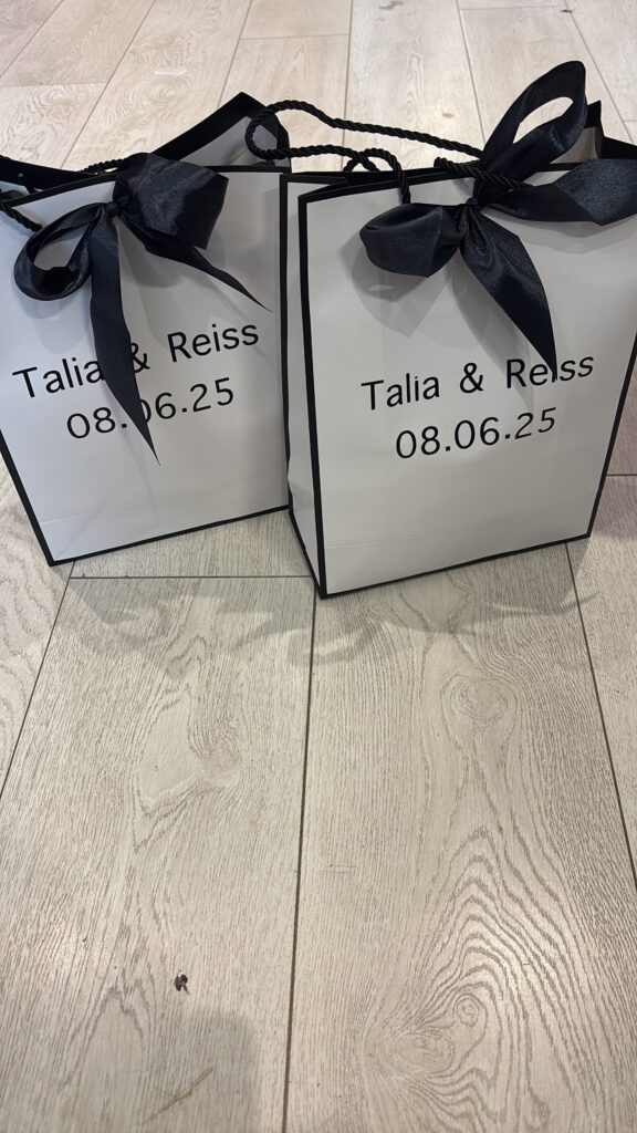 Two black gift bags with ribbons on a wooden surface