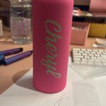 Pink sports insulated water bottle with 'Cheryl' branding in a casual indoor setting