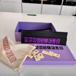 Gramsikub game set with purple box, wooden tiles, and drawstring bag on a white surface.