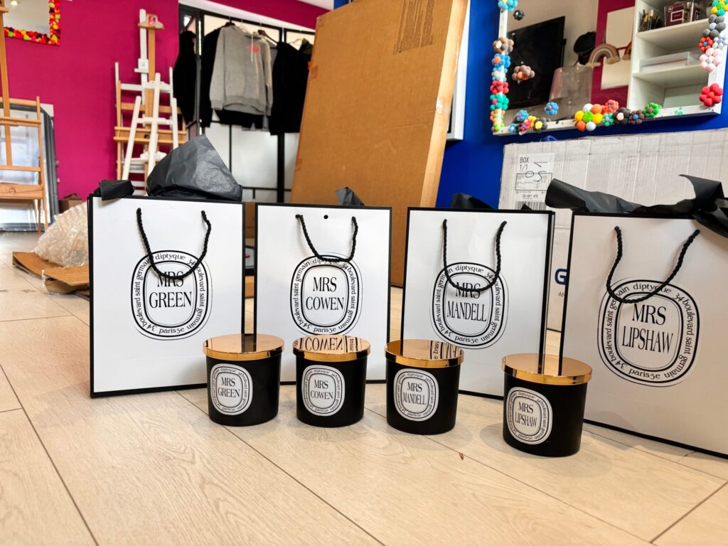 Set of branded gift bags and containers on a wooden floor with colourful decorations in the background.