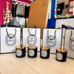 Set of branded gift bags and containers on a wooden floor with colourful decorations in the background.