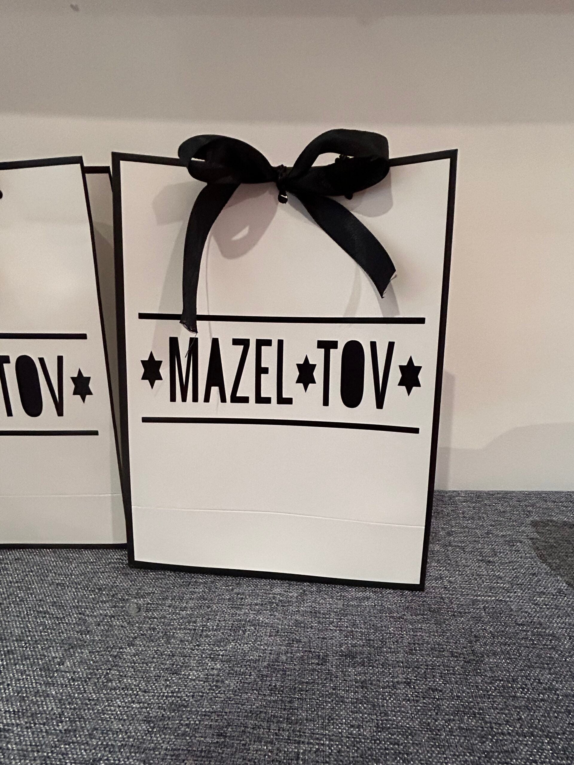 Gift bag with 'Mazel Tov' text and a black bow on a grey surface.