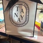 Gift bag with a black bow and 'TANYA' branding on a store shelf.
