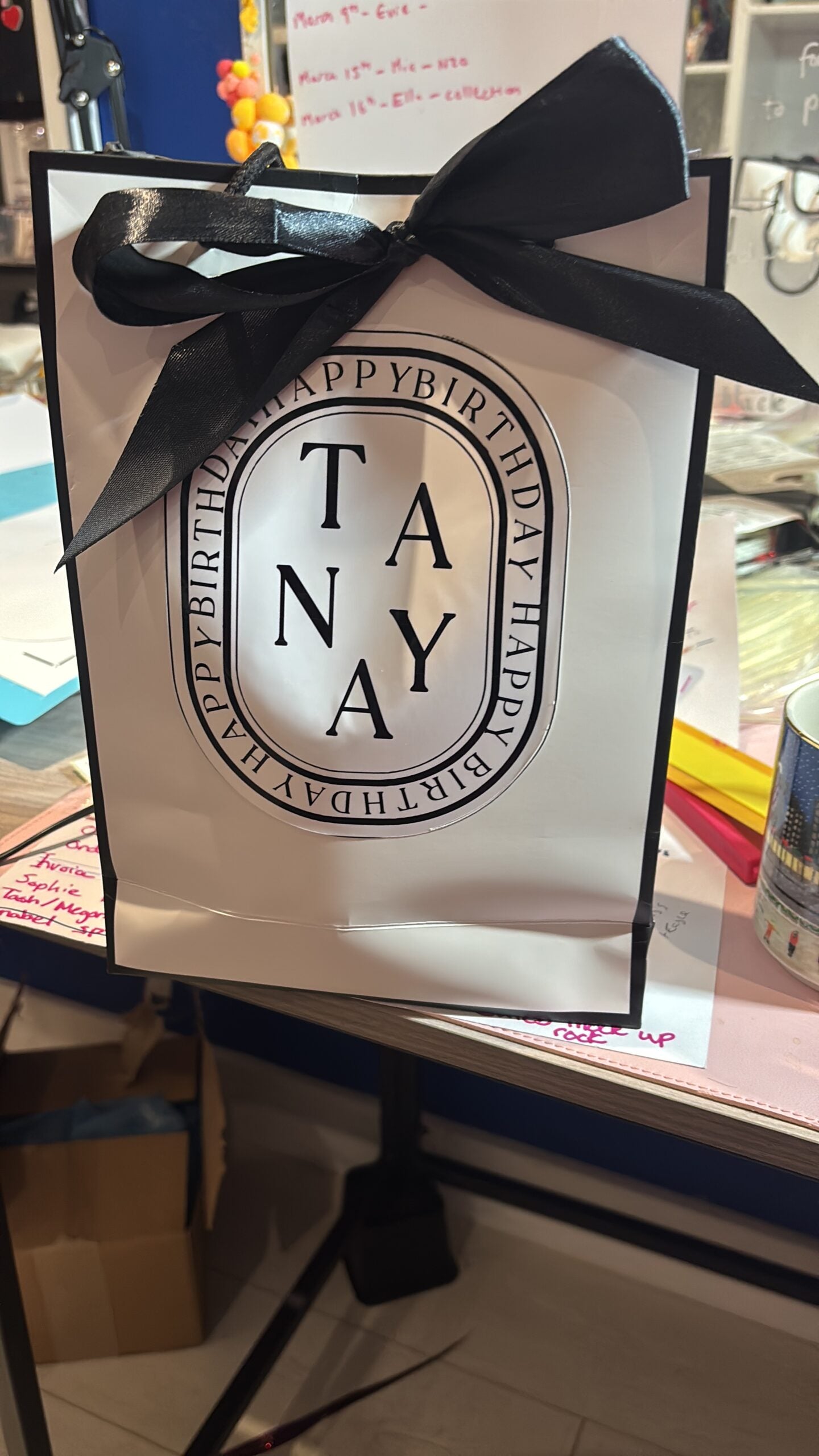 Gift bag with a black bow and 'TANYA' branding on a store shelf.