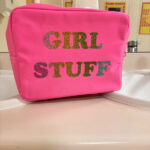 Pink washbag with 'GIRL STUFF' text in multicolour on a white surface.