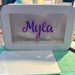 White washbag with 'Myla' printed on a clear window, on a green cutting mat.