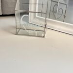 Glass gift card box with 'Natalia' engraved on a light-coloured floor.