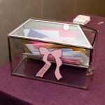 Glass gift card box with pink bow on a purple tablecloth