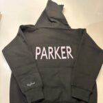 Dark grey hoodie with 'PARKER' printed on the back, laid flat on a light surface.
