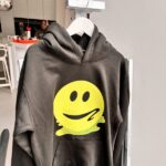 Grey hoodie with a yellow smiley face design on a hanger in a kitchen.