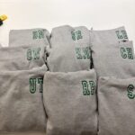 Stack of grey sweatshirts with green lettering on a white background
