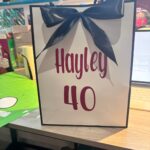 Gift bag with 'Hayley 40' text and a blue bow on a table.