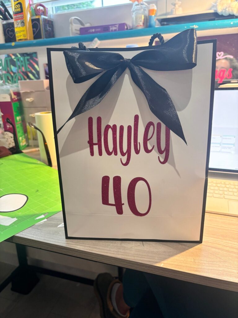 Gift bag with 'Hayley 40' text and a blue bow on a table.