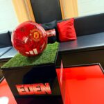 Red football labelled 'Manchester United' on a black stand with 'EDEN' written on it, placed on grass as a gift card box