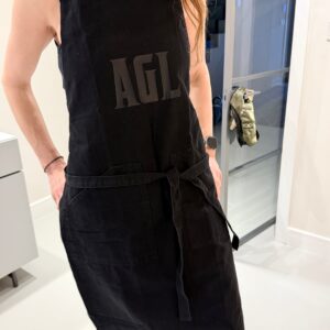 Person wearing a personalised black apron with a logo, standing indoors.
