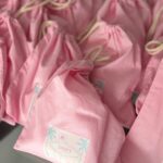 Pink drawstring personalised tote bags with labels on a reflective surface