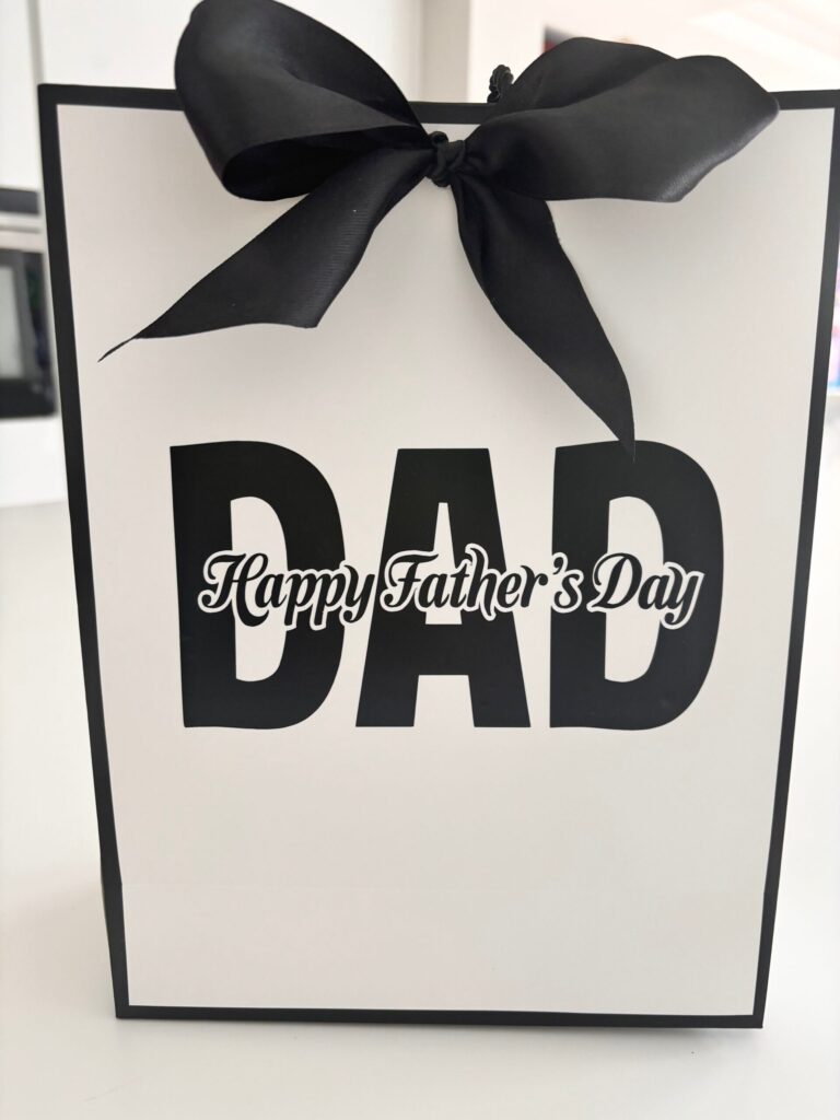Gift bag with 'DAD' and 'Happy Father's Day' text, tied with a black ribbon.