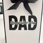Gift bag with 'DAD' and 'Happy Father's Day' text, tied with a black ribbon.