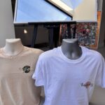 White and beige event t-shirt with a logo on a table next to a computer screen