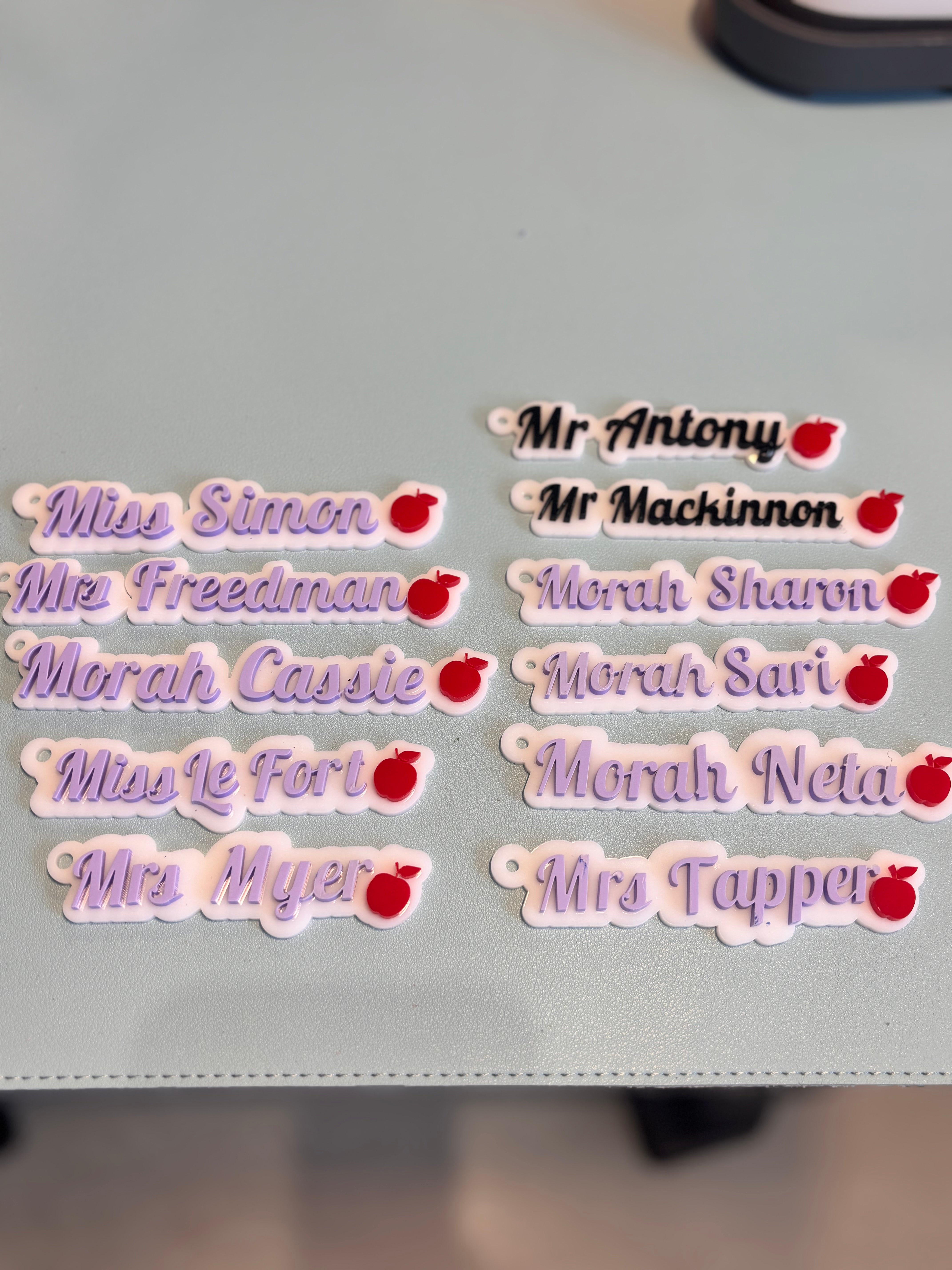 Keyrings with names and small red apple design on a grey surface