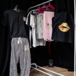 Clothing rack with various pyjamas such as shirts and pants on a wooden floor against a black wall.