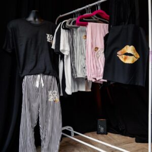 Clothing rack with various pyjamas such as shirts and pants on a wooden floor against a black wall.