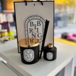 Personalised 'Bibring' candle and diffuser set with gold lids on a white surface, with a branded bag in the background.