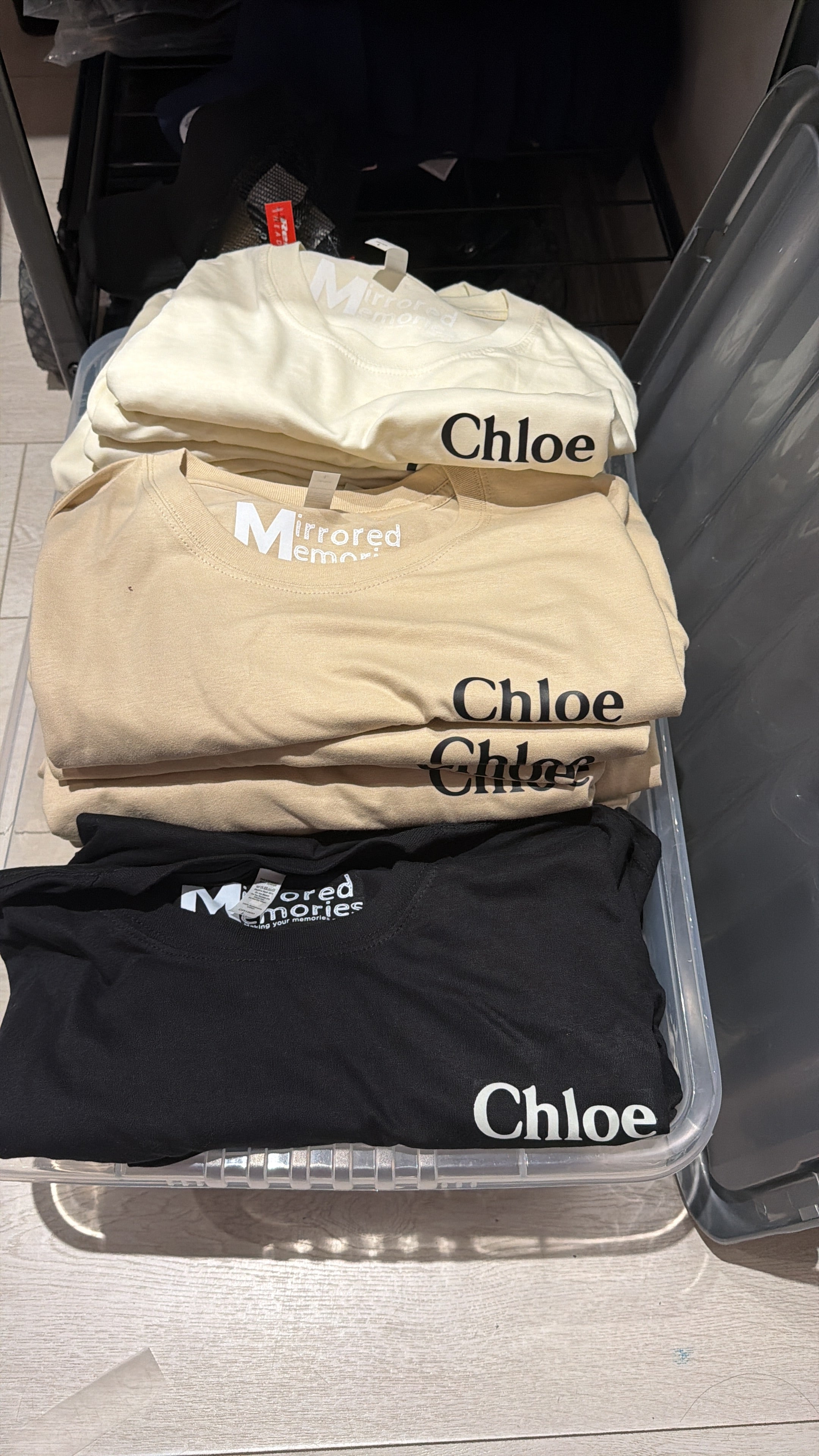Personalised Chloe event t-shirts in a clear plastic container on a light-coloured surface