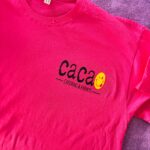 Pink event t-shirt with 'Caca' logo on a purple surface