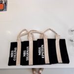 Set of black personalised tote bags with white text on a white surface
