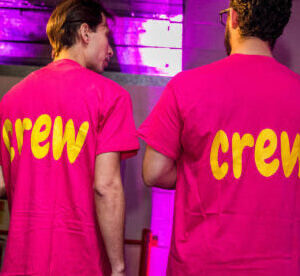 Two people wearing pink 'crew' personalised t-shirts in a dimly lit room with purple lighting.