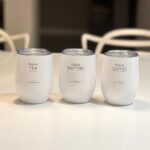Three white travel cups labelled 'this is TEA', 'this is MATCHA', and 'this is COFFEE' on a light surface.