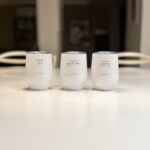 Three white travel cups labelled 'this is TEA', 'this is MATCHA', and 'this is COFFEE' on a blurred light surface.