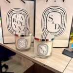 Two Diptyque-style candles on a wooden surface with visible branding.