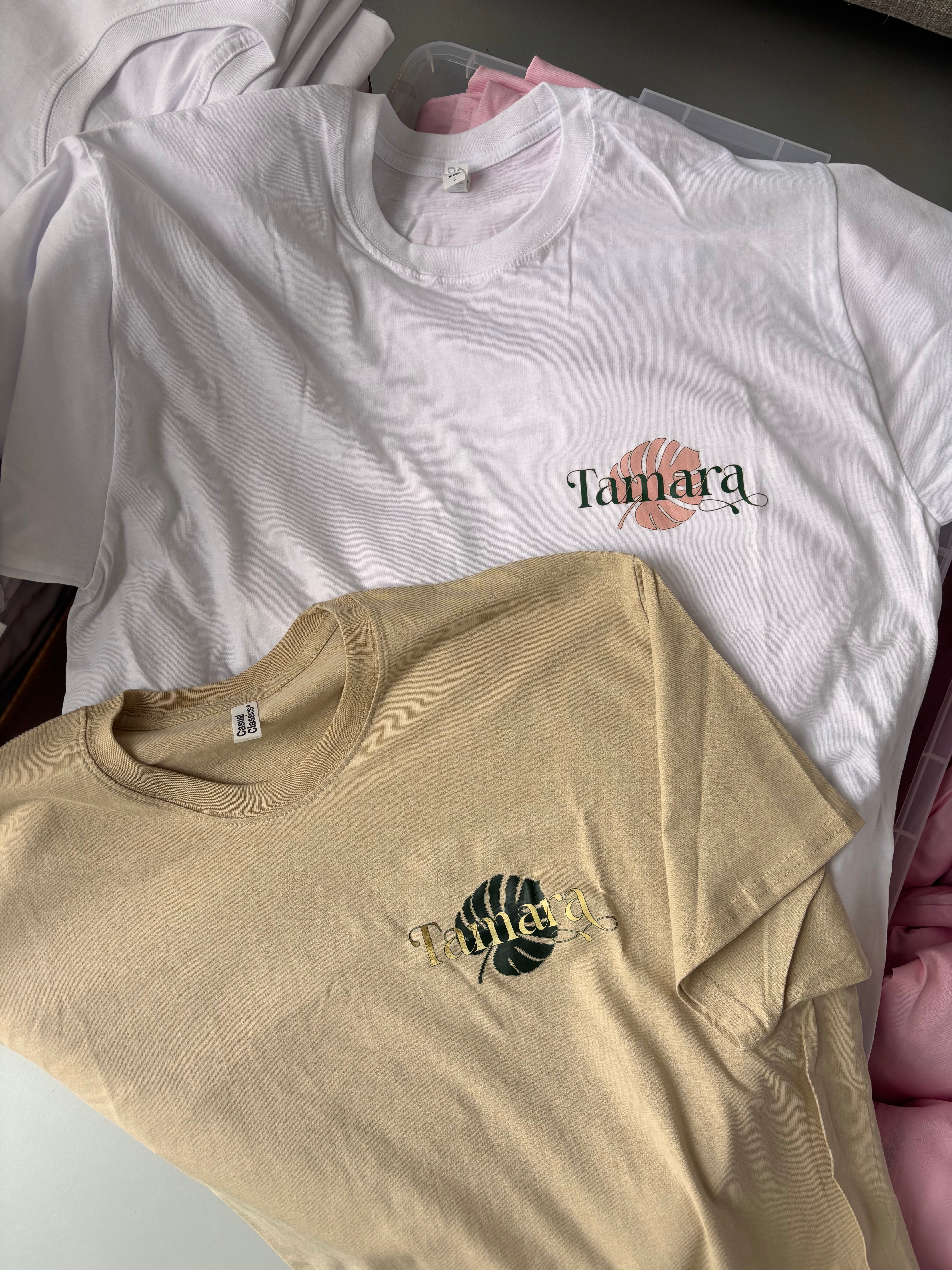 Two event t-shirts, one white with a logo and one beige with a different logo, on a surface.