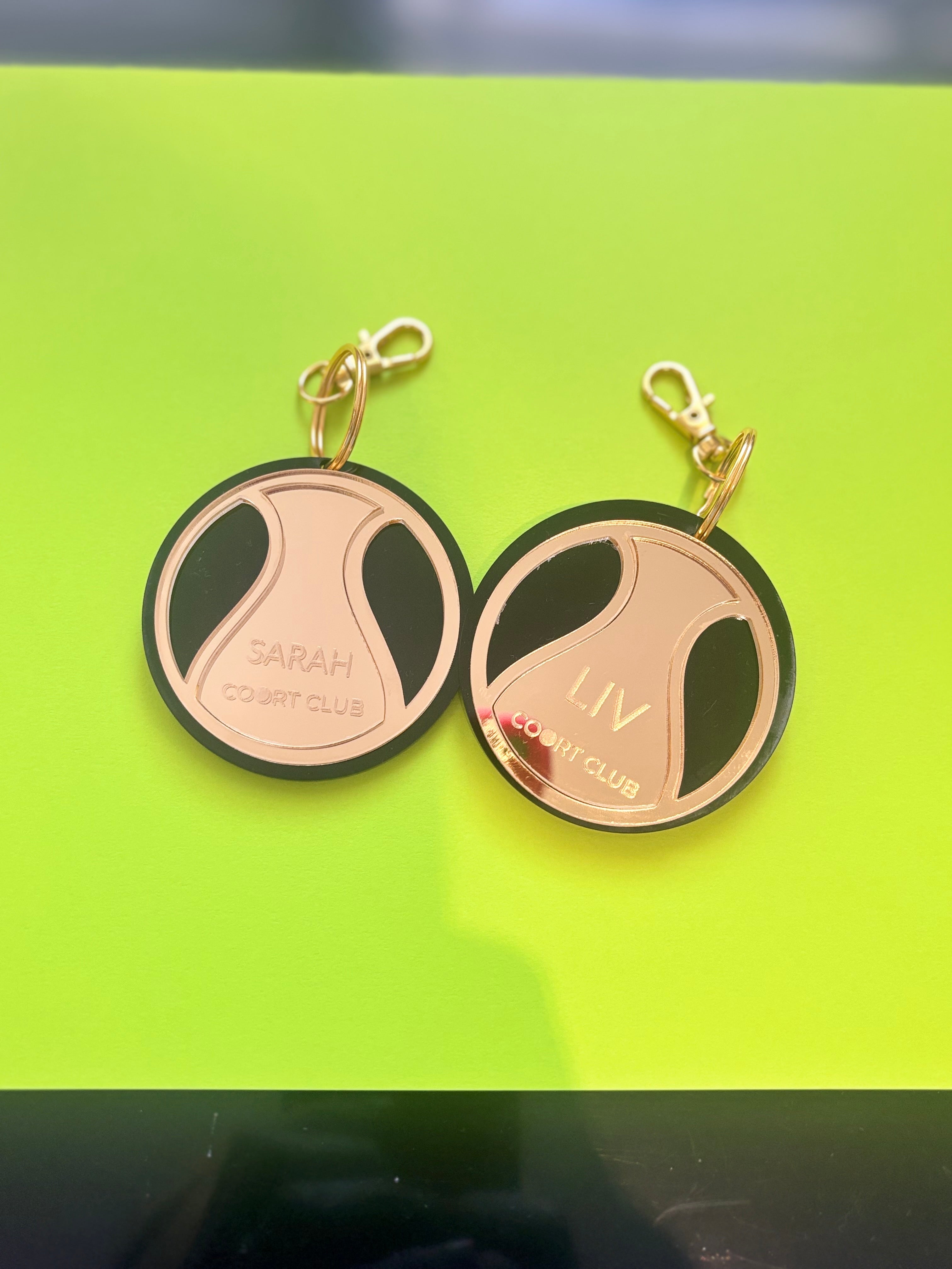 Two round keyrings with gold accents on a green background with personalised names in acrylic