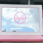 White framed classic mirror with 'Sophie' on pink acrylic.