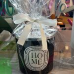 Diptyque-style 'Home' candle wrapped in cellophane with a ribbon on a blurred background