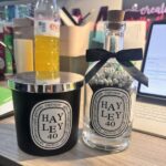 A candle and diffuser set with 'HAYLEY 40' labels on a desk.