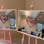 Two classic mirrors on pink stands with 'Lulu' and 'Mollie' written in hearts, in an office setting.