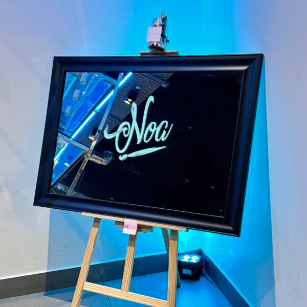 Black-framed_bespoke_mirror_on_an_easel_with_Noa_in_cursive_against_a_blue_wall.