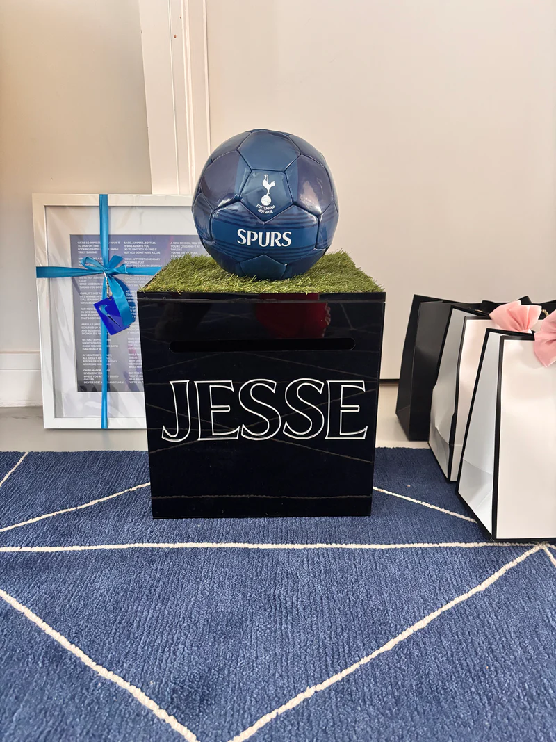 Black_gift_card_box_with_JESSE_printed_on_it_next_to_a_blue_ball_and_a_framed_picture_on_a_blue_textured_surface.