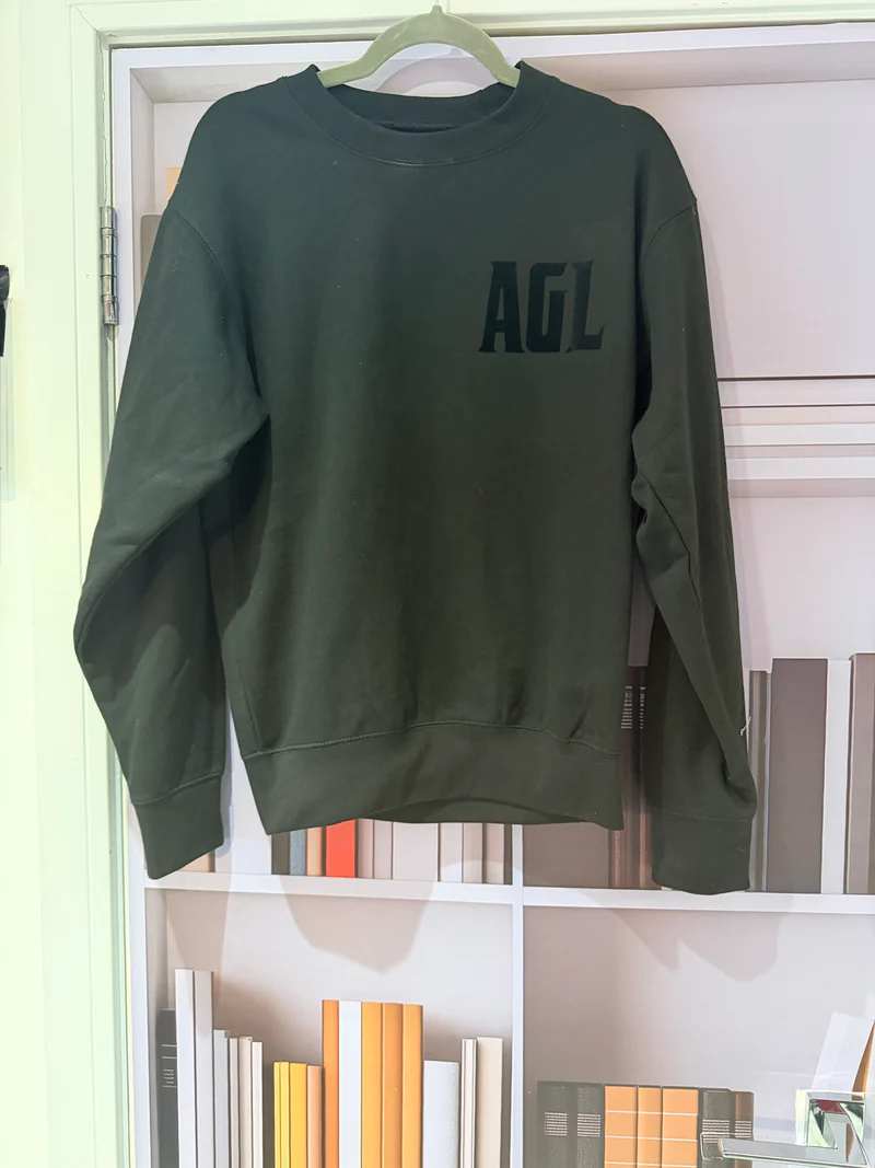 Green_long-sleeve_crewneck_shirt_with_AGL_logo_on_a_hanger_against_a_bookshelf_background
