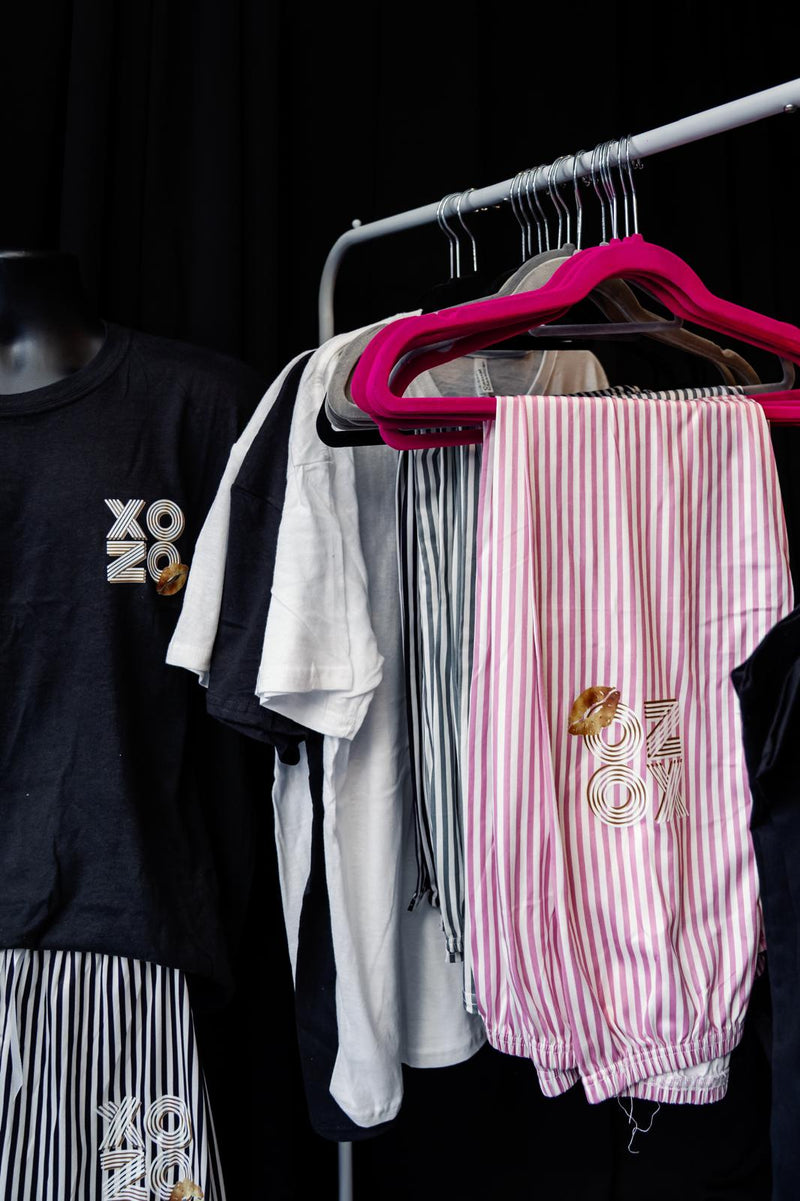 Pyjama_clothing_items_including_a_black_t-shirt_with_XO_logo_white_t-shirt_pink_striped_pants_and_a_black_jacket_on_a_rack.