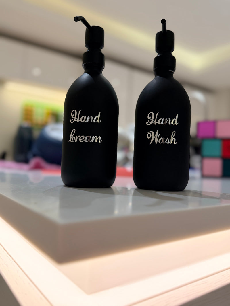 Two_black_soap_bottles_labelled_Hand_Lotion_and_Hand_Wash_on_a_reflective_surface.